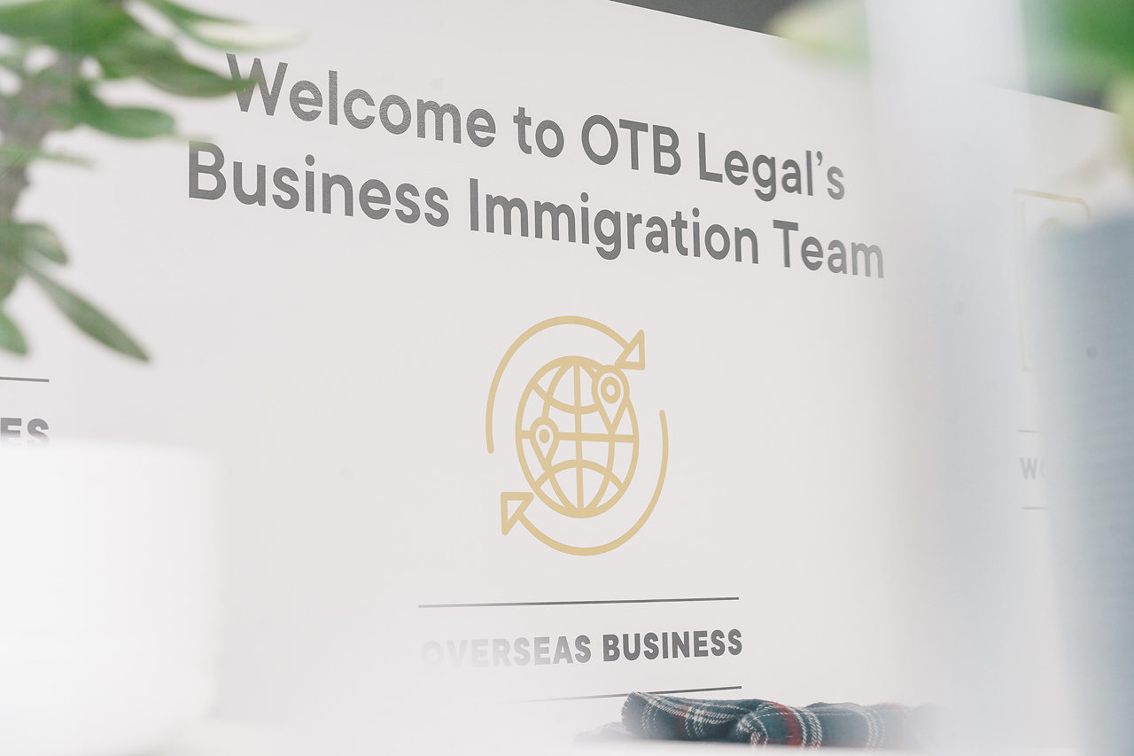 Business Immigration Team Logo printed on the office wall with a plant at the side