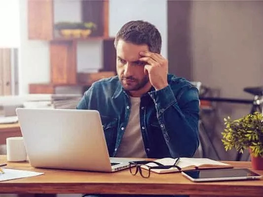 Homem sentado em frente ao laptop pensando
