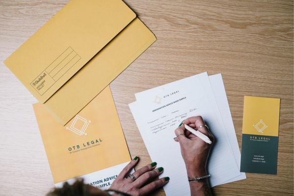 Dépliants juridiques d'OTB et écrit d'une femme. Suppression de la procédure de résidence de 10 ans pour l'obtention du titre de séjour permanent